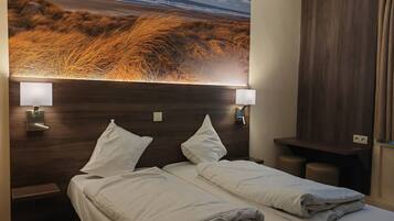 A hotel room with two beds, a large wall mural of a beach, and two bedside lamps.