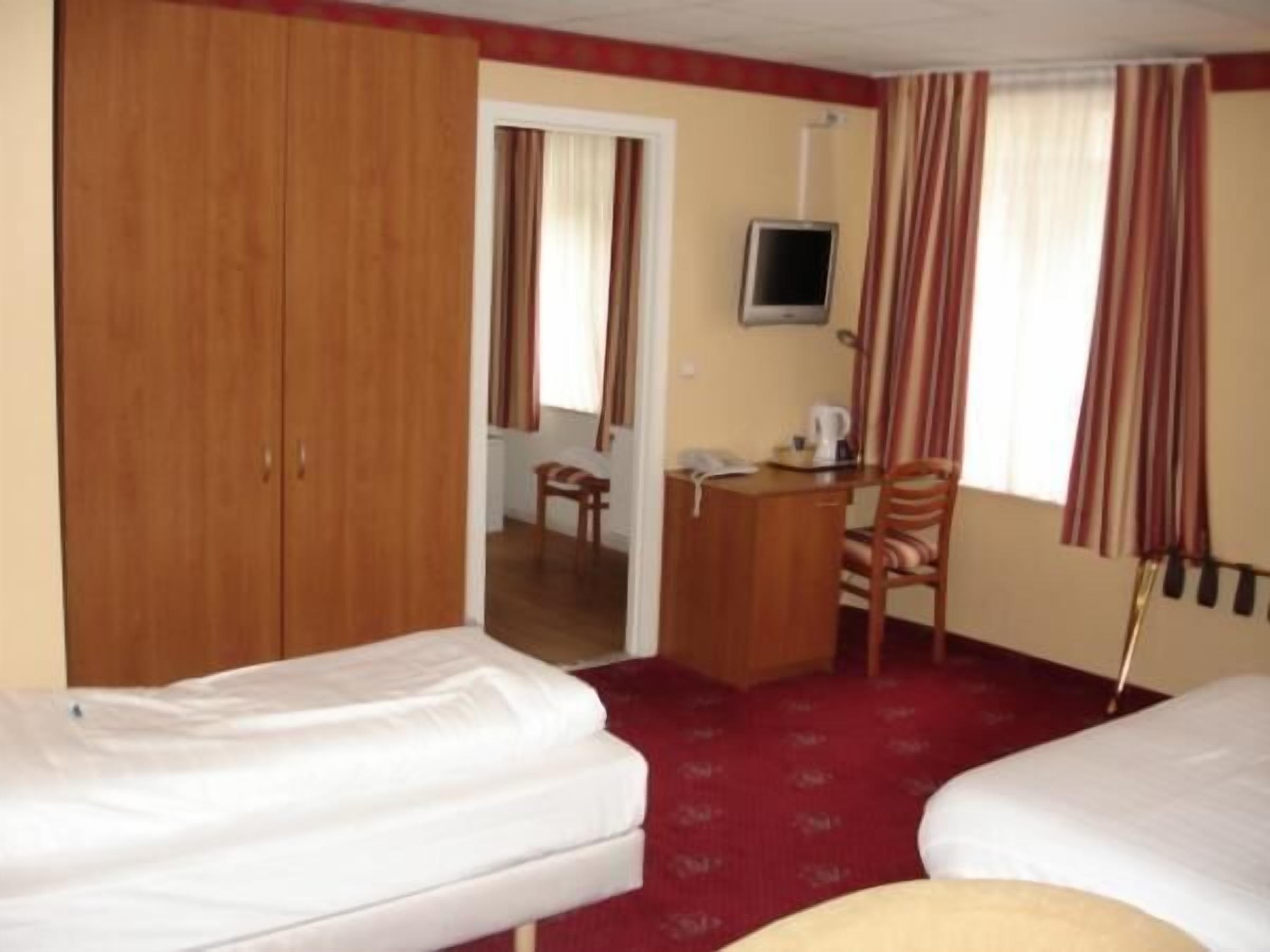 A hotel room with two beds, a desk with a chair, a television, and a wardrobe.