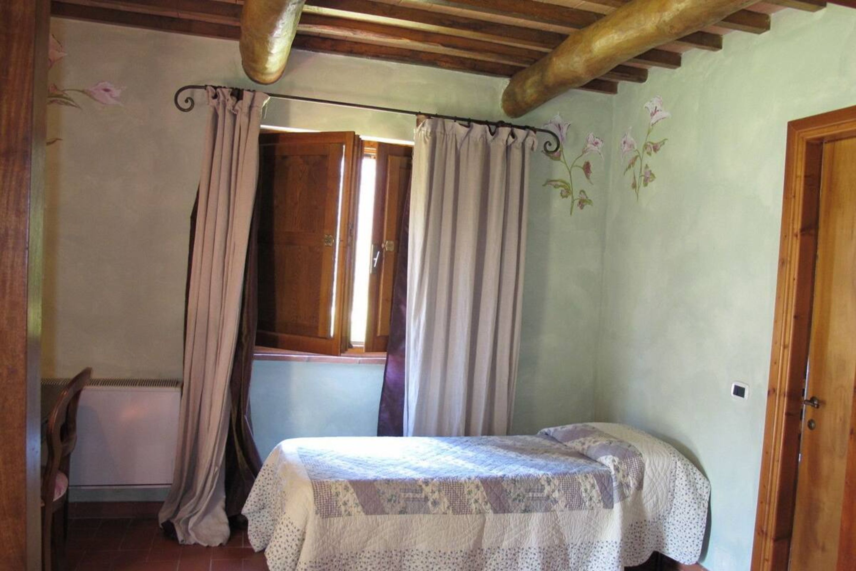 Ein kleines, gemütliches Schlafzimmer mit einem Einzelbett, Holzbalkendecke und einem Fenster mit Vorhängen.