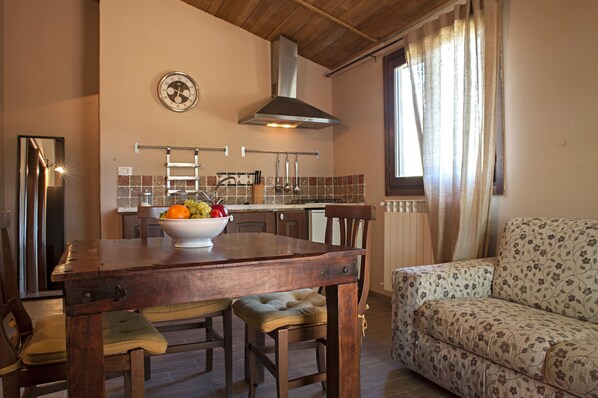 A kitchen with a wooden table, a bowl of fruit, and a dining chair. - Relais Ciavatta Country Hotel (Manciano)