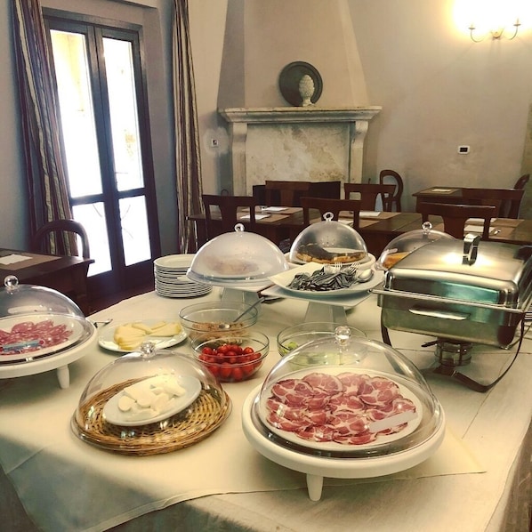 Una mesa de buffet con diversos alimentos cubiertos por campanas de cristal, incluyendo carnes, quesos y frutas.