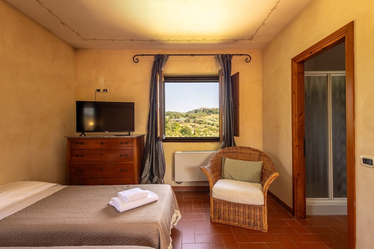 A bedroom with two beds, a TV, a wicker chair, a window with a view, and a door.