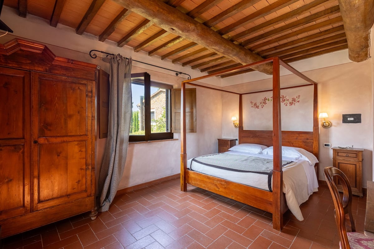 A bedroom with a four-poster bed, wooden wardrobe, and a window with curtains.