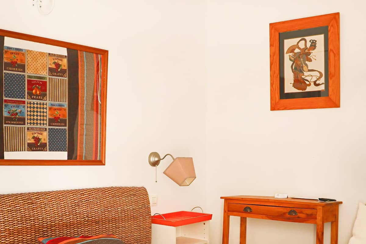 Une chambre à coucher bien rangée, avec un lit, une table de chevet, une lampe et un tableau encadré au mur.