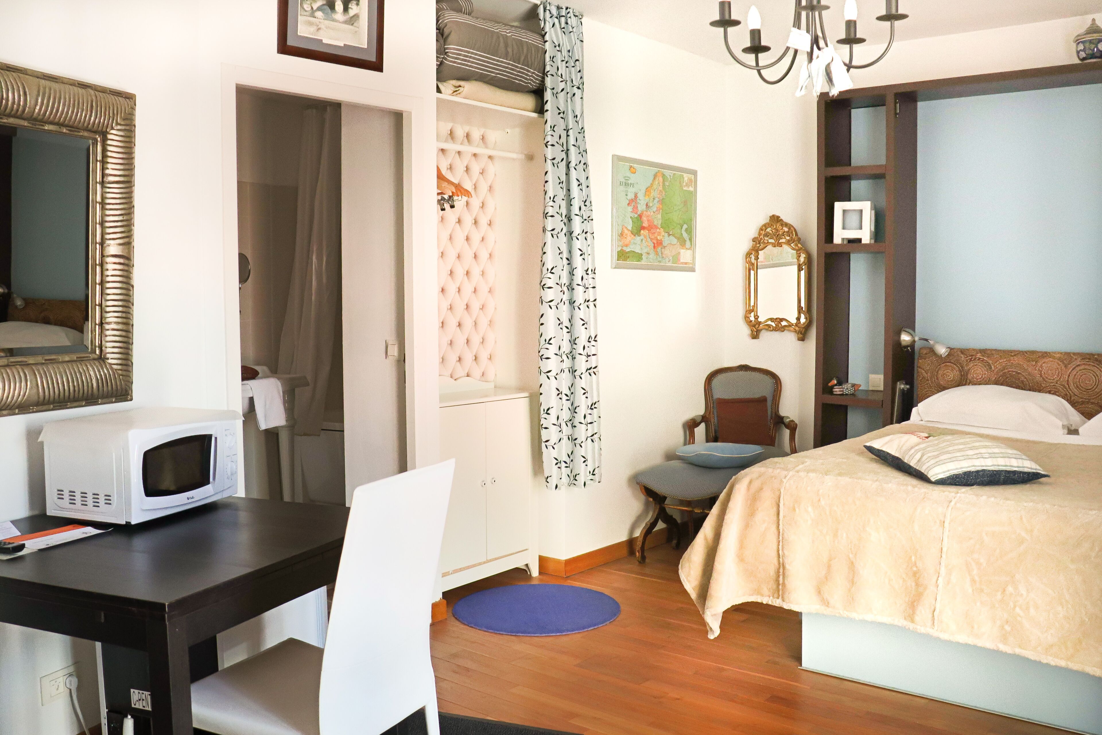Quarto com cama, escrivaninha com micro-ondas, cadeira, guarda-roupa e lustre.