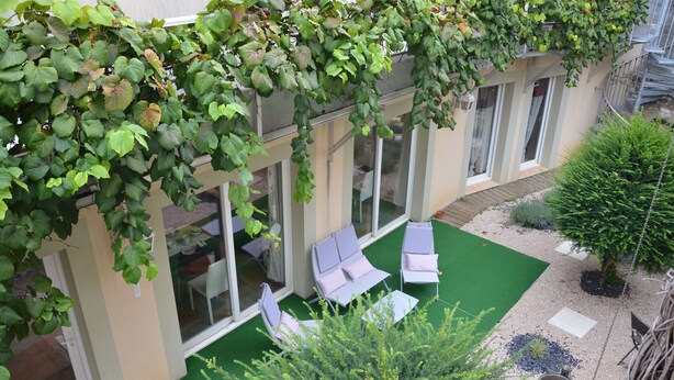 Un patio techado con mobiliario exterior, una zona de césped artificial verde y diversas plantas.