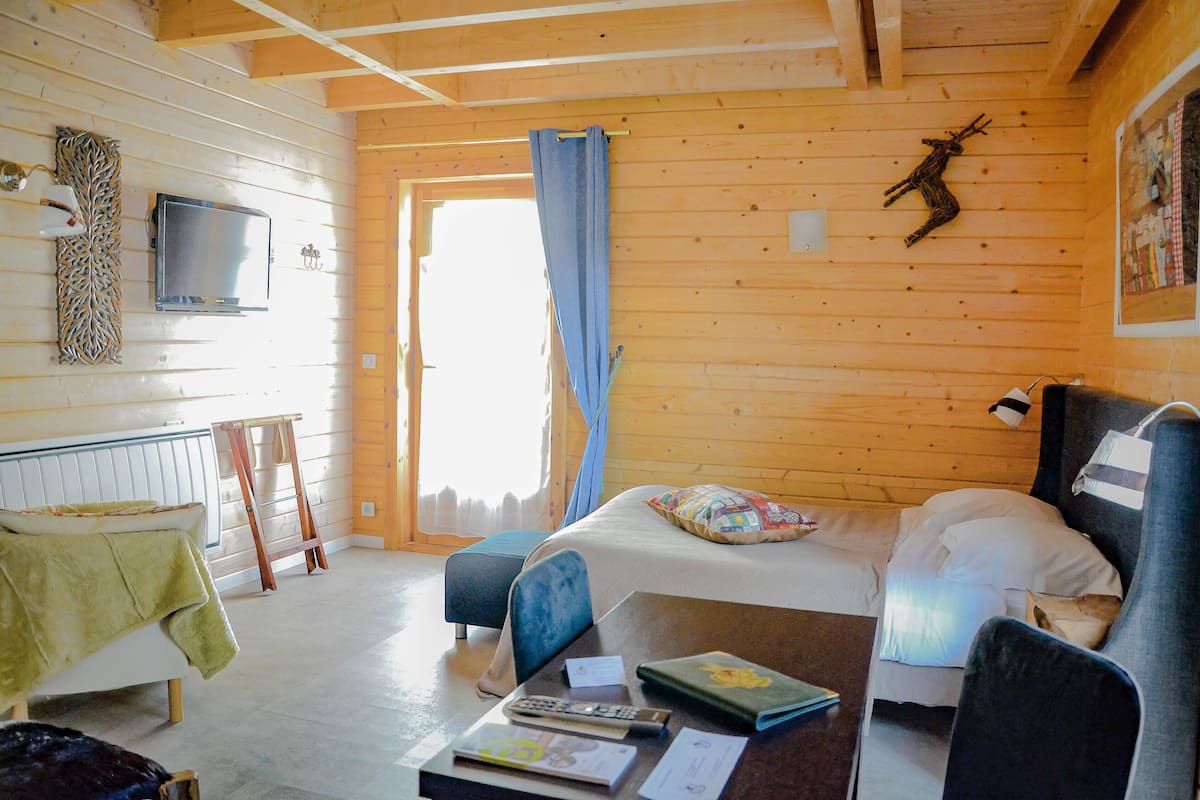Une pièce de cabane en bois comprenant un lit, une table avec des livres, une chaise, un téléviseur et un plafond en bois.