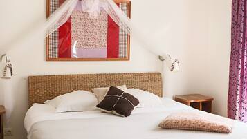 Quarto com cama, mesa de cabeceira, pequena mesa, luminária na parede e um objeto decorativo sobre a cama.