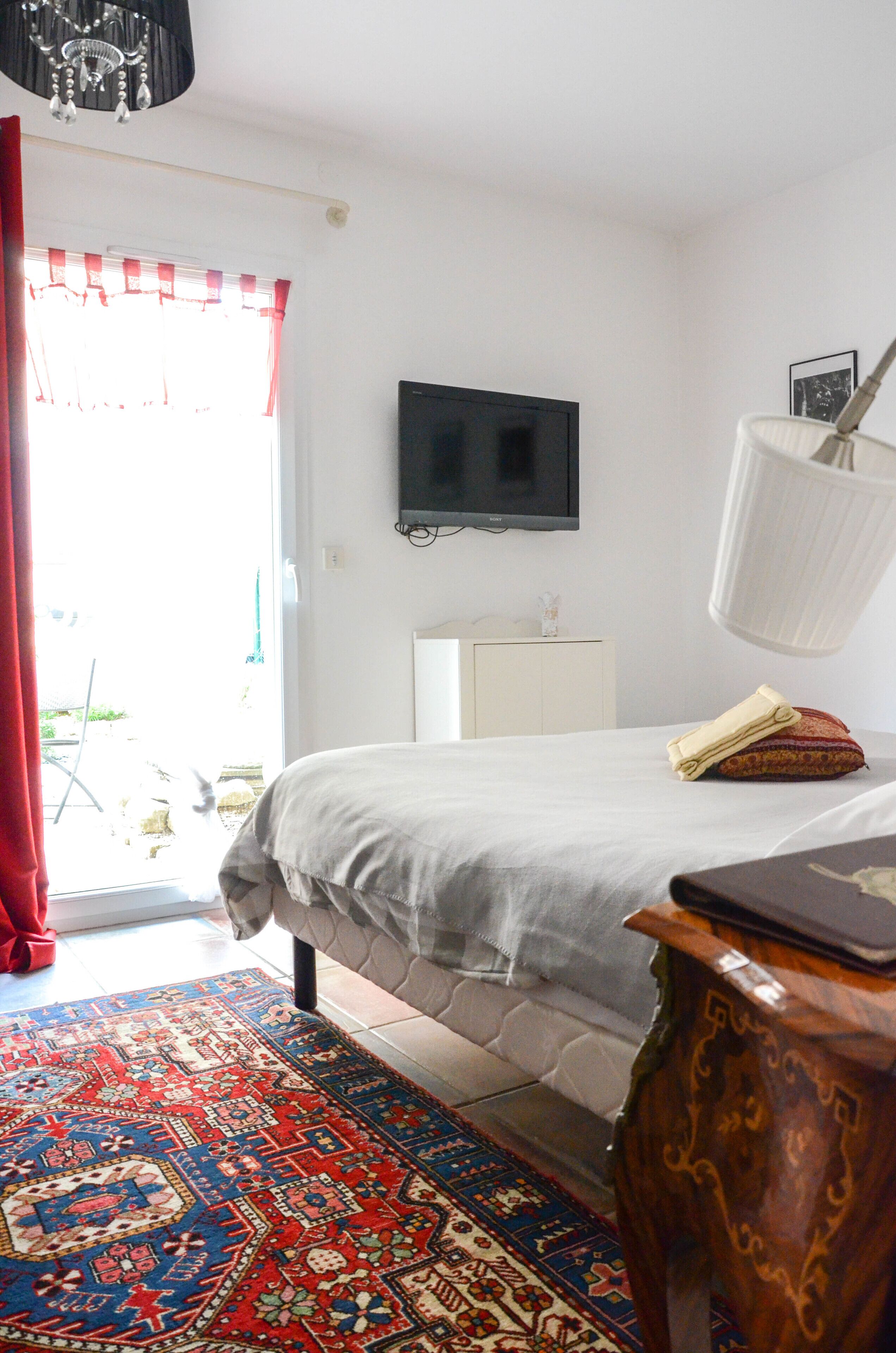 A bedroom with a bed, a television, a lamp, a desk, and a patterned rug.