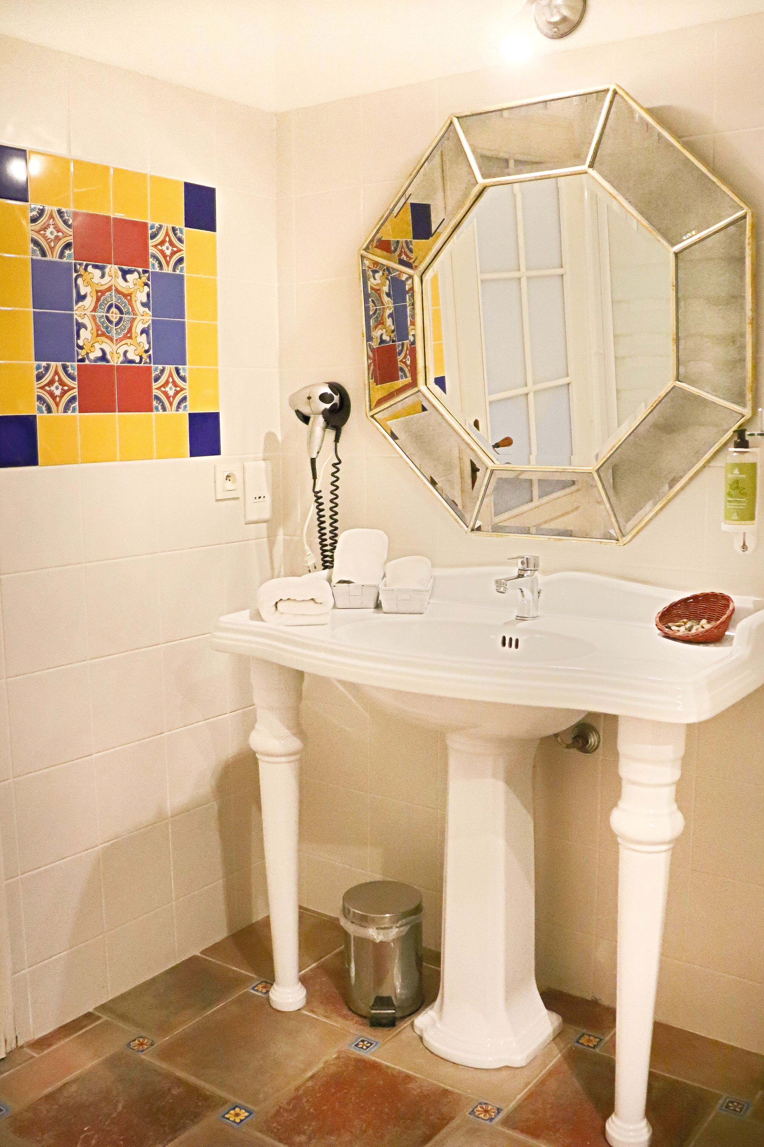 Un baño con un lavamanos blanco de pedestal, un espejo grande y un salpicadero de azulejos coloridos.