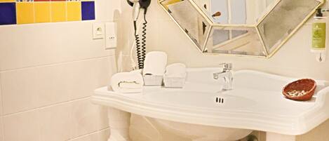 Un baño con un lavamanos blanco de pedestal, un espejo grande y un salpicadero de azulejos coloridos.