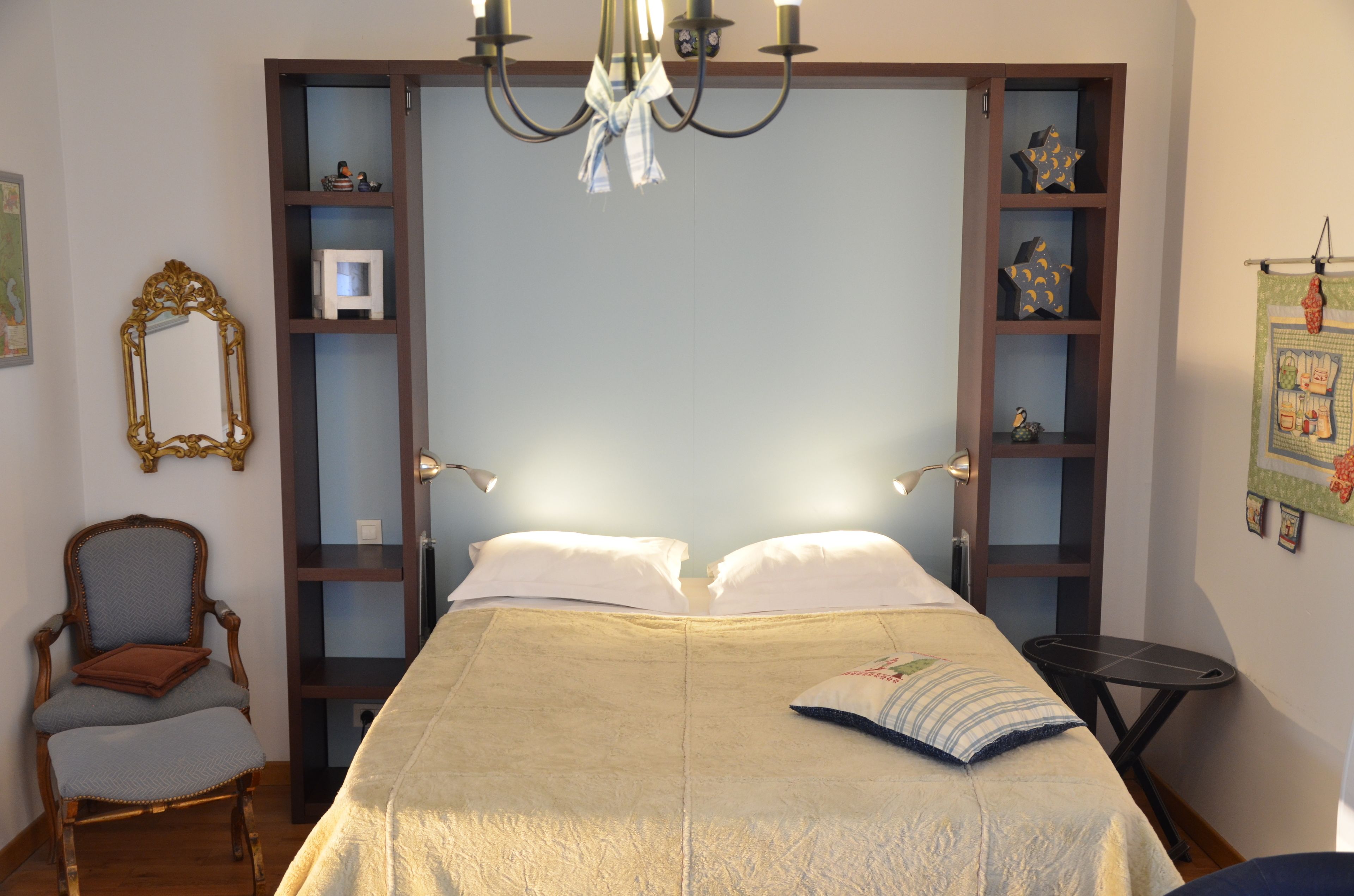 Un dormitorio con una cama grande, cabecera de madera, una lámpara de araña, una silla y una pequeña mesa.
