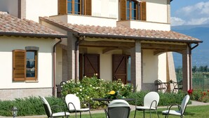 A two-story house with a patio area featuring outdoor seating and a view of the mountains. - Agriturismo Le Rondini di Francesco di Assisi (Cannara)