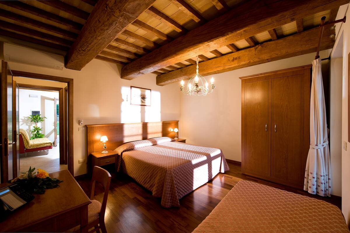 A bedroom with two beds, wooden beams, a chandelier, a desk with a lamp, and a wardrobe.