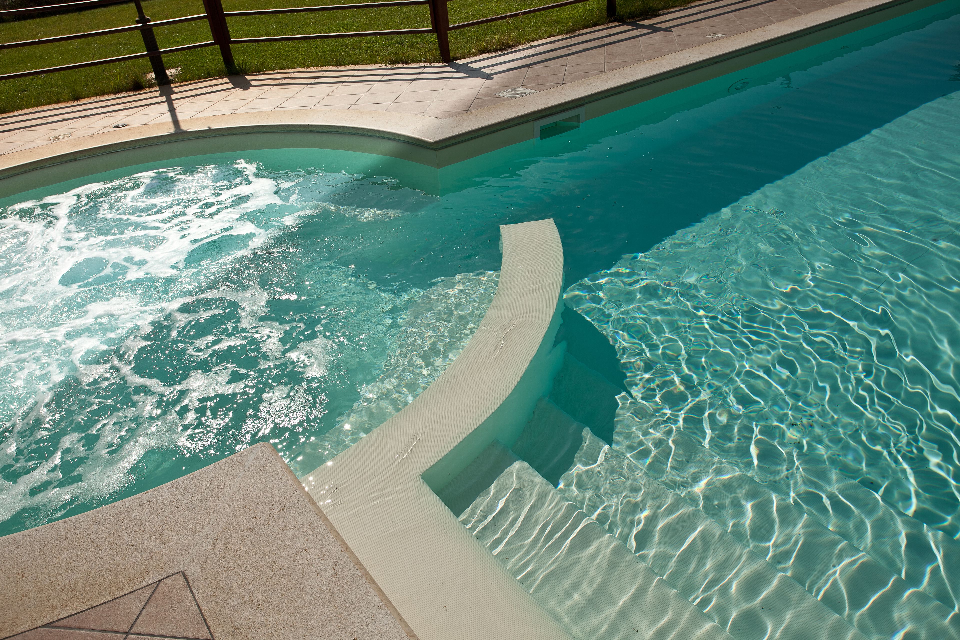 A swimming pool with clear water, a curved edge, and a tiled deck area.