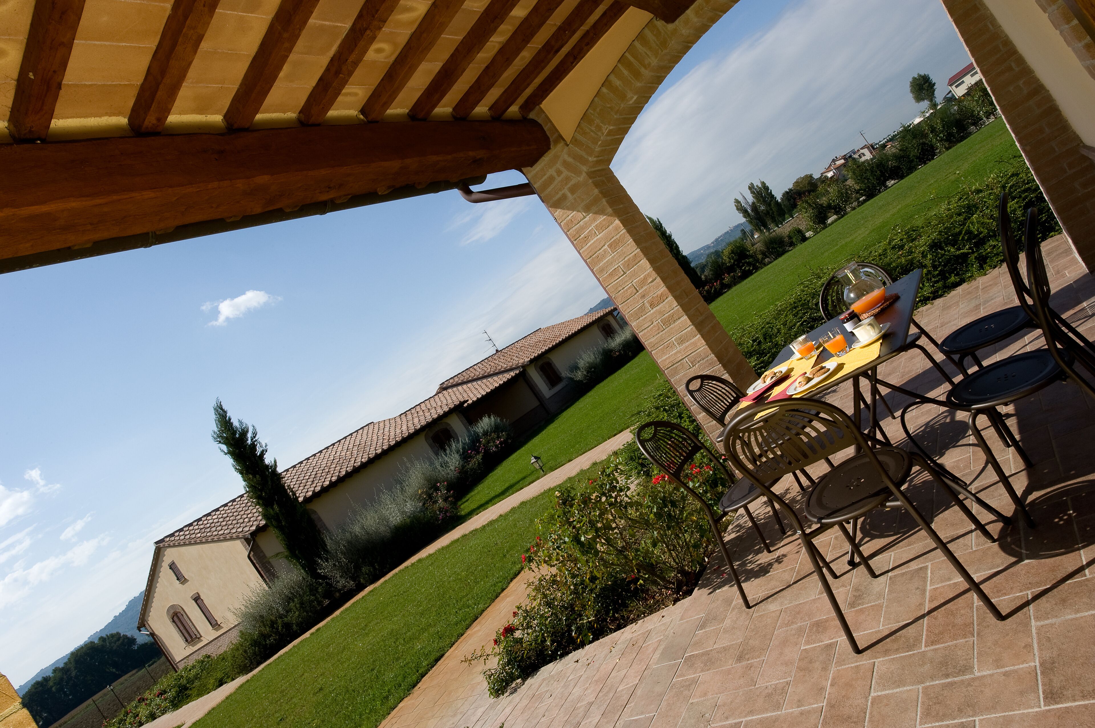 Un patio con mesa y sillas, una pérgola en lo alto y vista a una casa con techo de tejas.