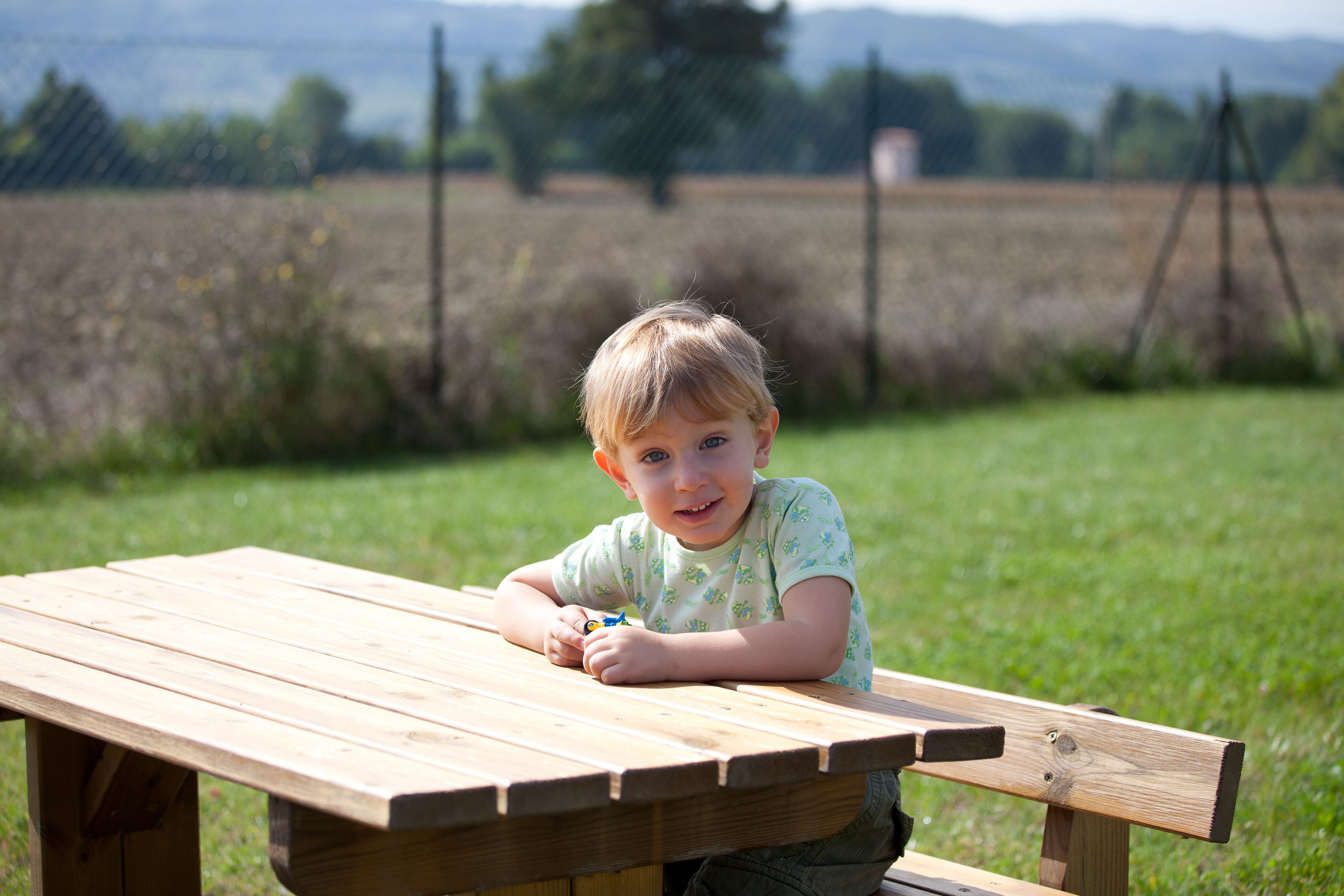 Een houten picknicktafel in een open landschap, met een grasveld en heuvels in de verte.
