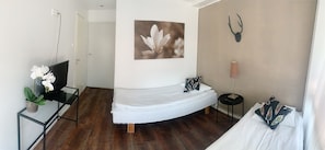 A compact room with a bed, a desk with a plant, a wall-mounted deer head, and a framed flower painting. - Hotel Harriet (Turku)
