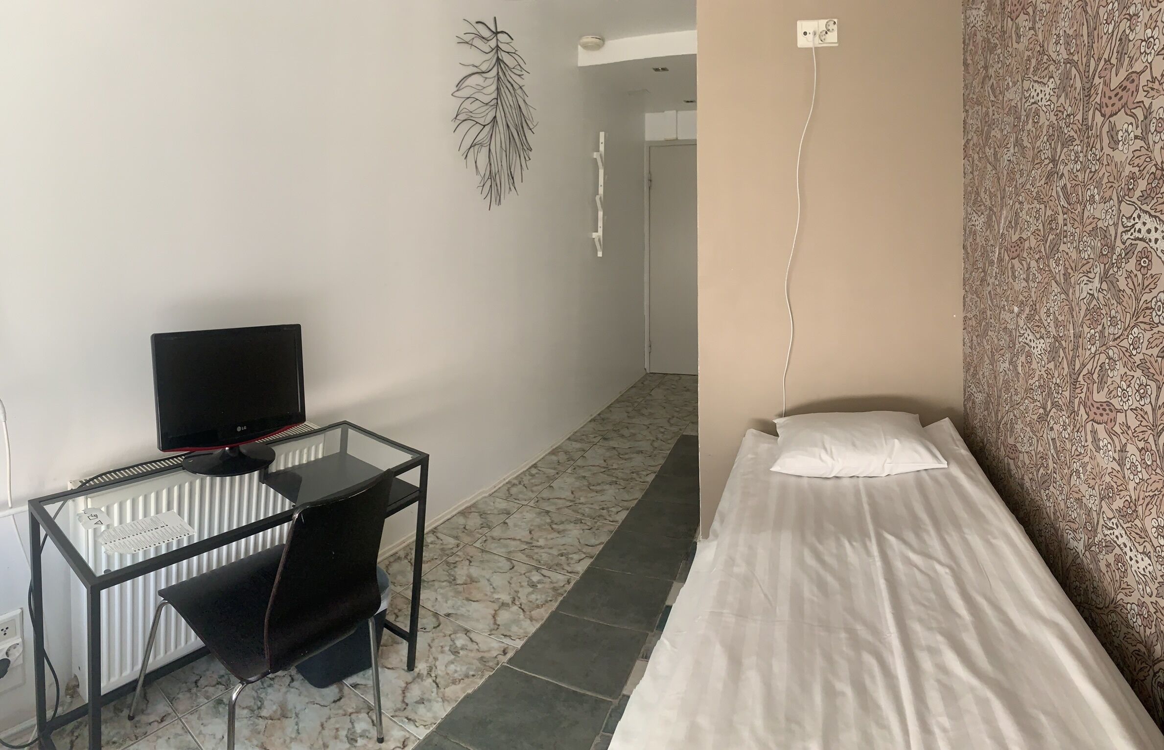 A small room with a single bed, a desk with a computer, and a radiator.