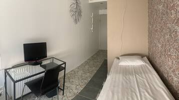 A small room with a single bed, a desk with a computer, and a radiator.