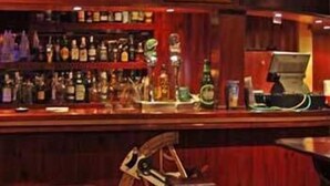 A bar area with shelves of liquor bottles, a cash register, and a cash register drawer. - Blue Beach (CAN PICAFORT)