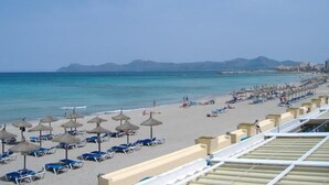 A beach with rows of sun loungers and umbrellas, a clear blue sea, and distant mountains. - Blue Beach (CAN PICAFORT)
