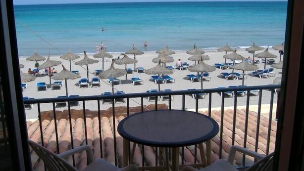 A balcony with a view of a beach, featuring lounge chairs, umbrellas, and a table. - Blue Beach (CAN PICAFORT)