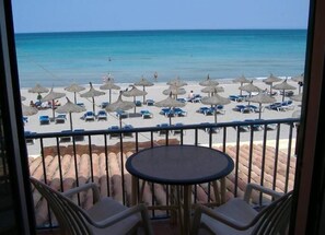 Ein Balkon mit Blick auf einen Strand, ausgestattet mit Liegestühlen, Sonnenschirmen und einem Tisch.