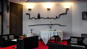 Eine Hotellobby mit rotem Teppich, schwarzen und weißen Sofas, einem Tisch mit weißem Tischtuch und einer Wand mit Skyline-Silhouette.