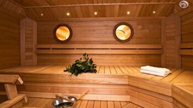 Een houten sauna met banken, een bank met een handdoek en een kom.