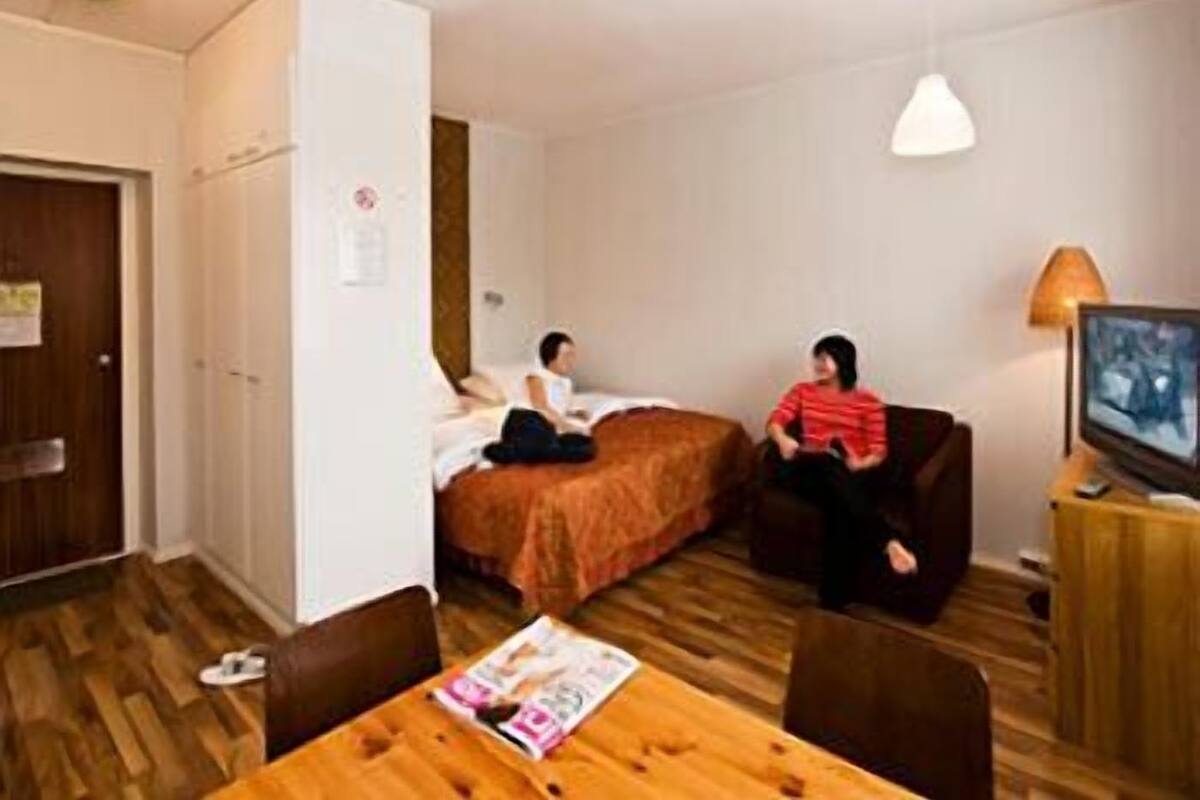 A small, well-lit room with two beds, a wooden table, and a television.