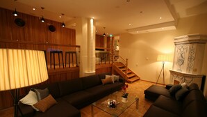 Een moderne woonkamer met een donkerbruine bank, een glazen salontafel en een houten trap die naar een verdieping leidt.