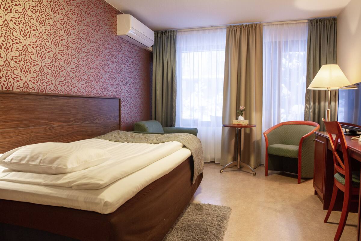 Habitación de hotel con cama, escritorio, silla y una mesita.