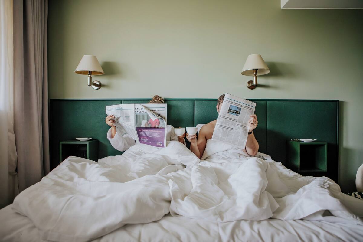 Una habitación de hotel con cabecera verde, dos mesitas de noche con lámparas y una cama con ropa blanca.