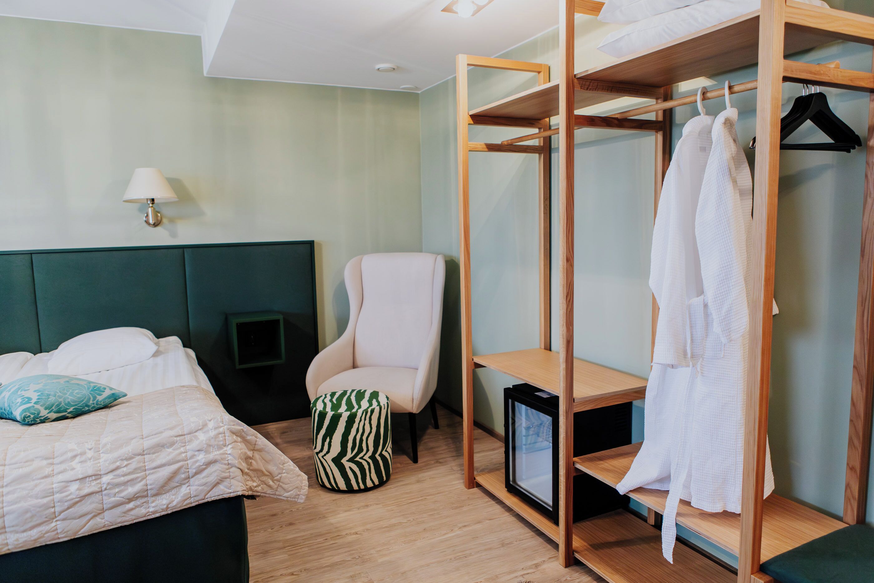 Quarto de hotel com uma cama, uma cadeira, um guarda-roupa e uma mesa pequena.