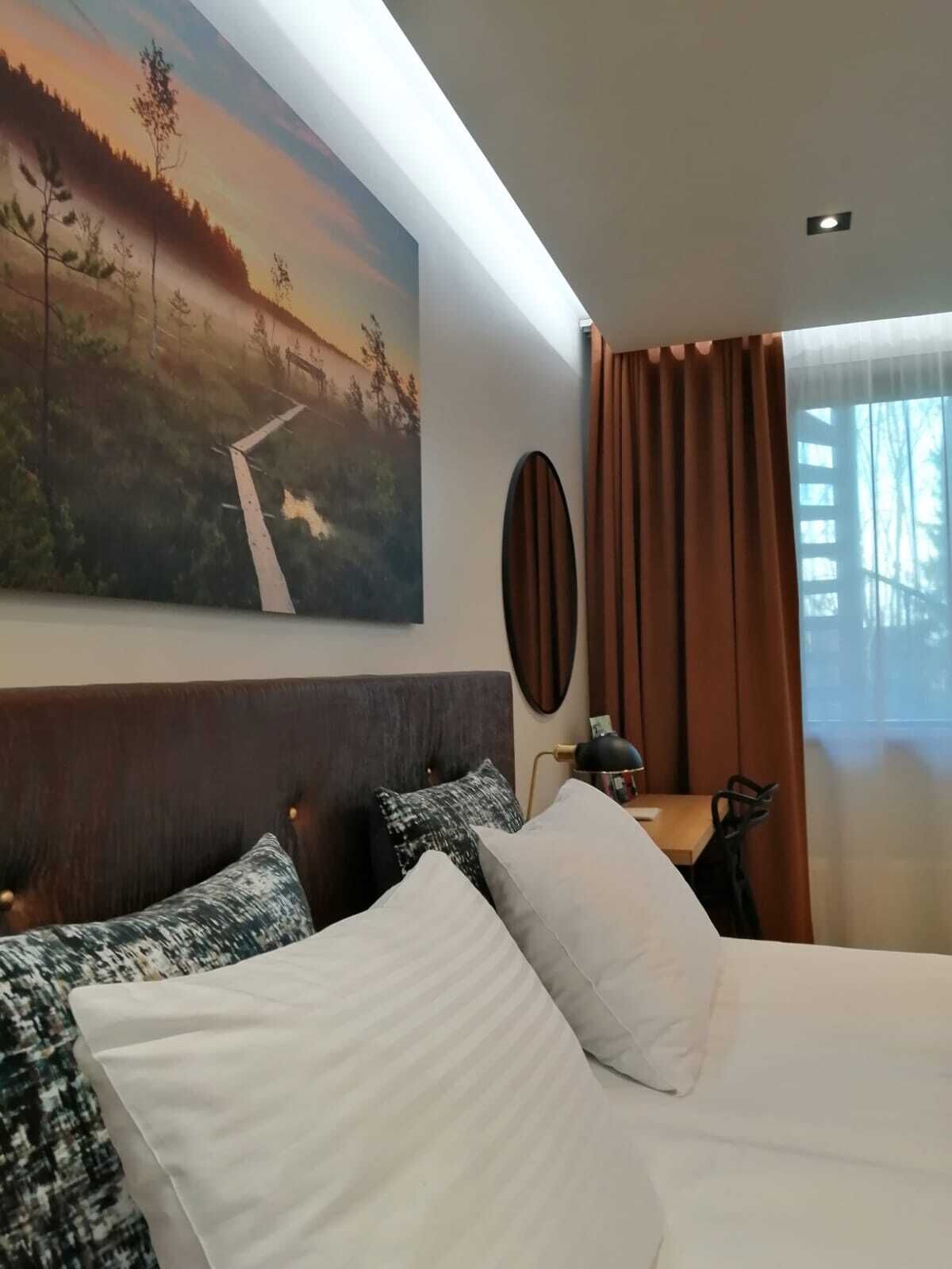 A hotel room with a large bed, a desk, a chair, a painting on the wall, and a window with curtains.