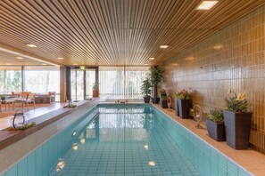 Une piscine aux murs et au plafond recouverts de carreaux, entourée de plantes en pot et agrémentée d’espaces de détente.