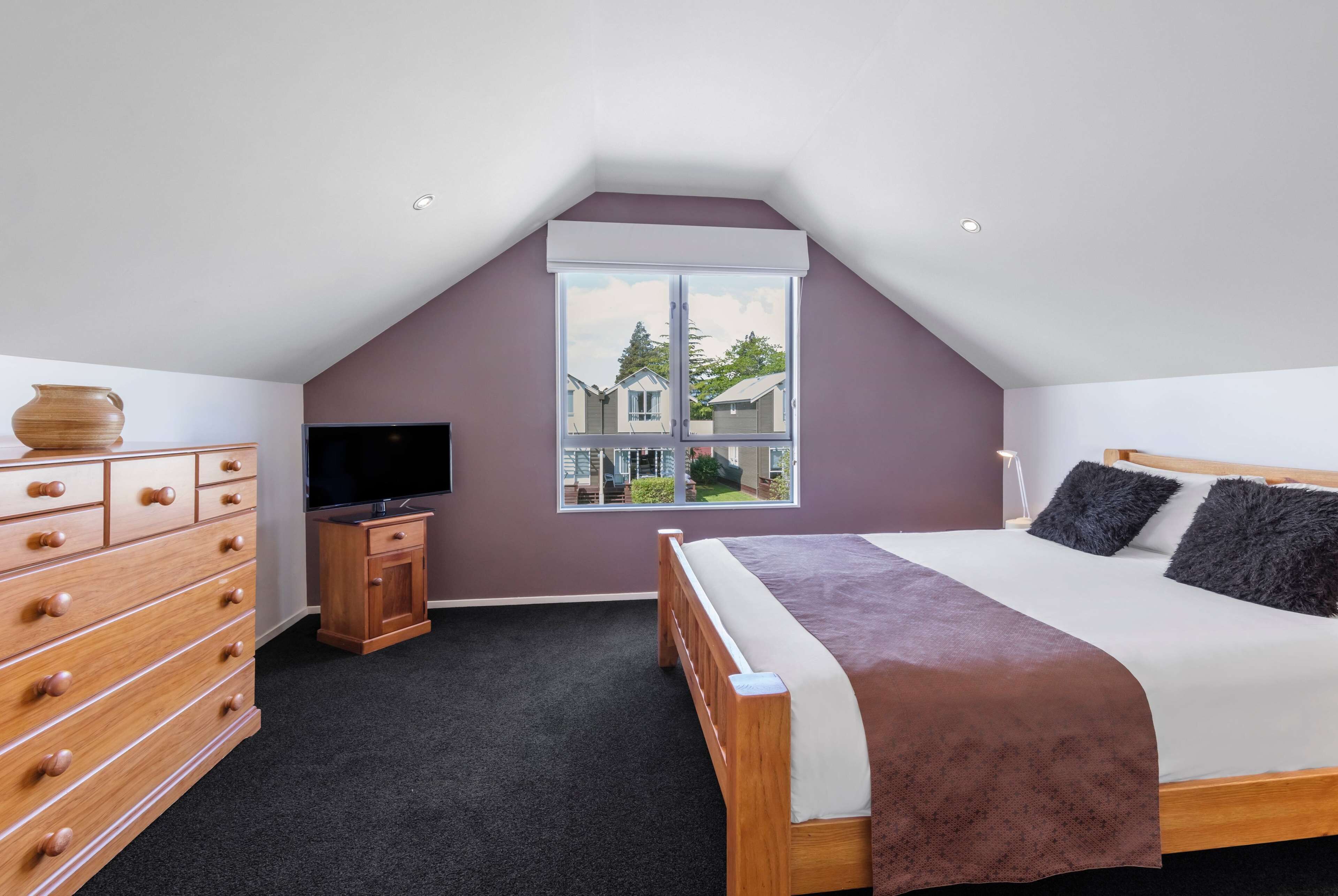 Een slaapkamer met een schuine hemel, een groot raam, een bed, een dressoir en een televisie.