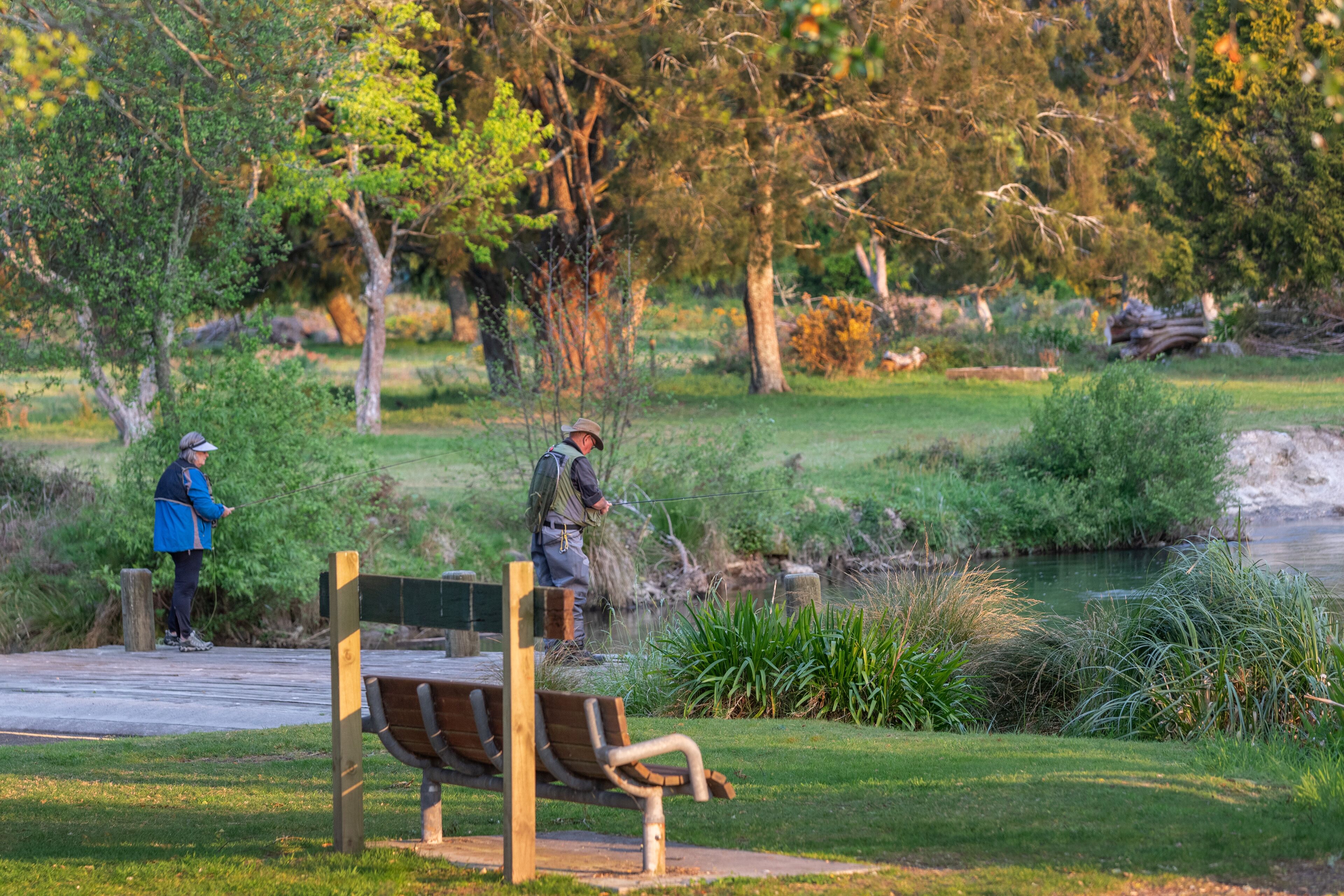 A park with a wooden bench, a pond, and two people walking.