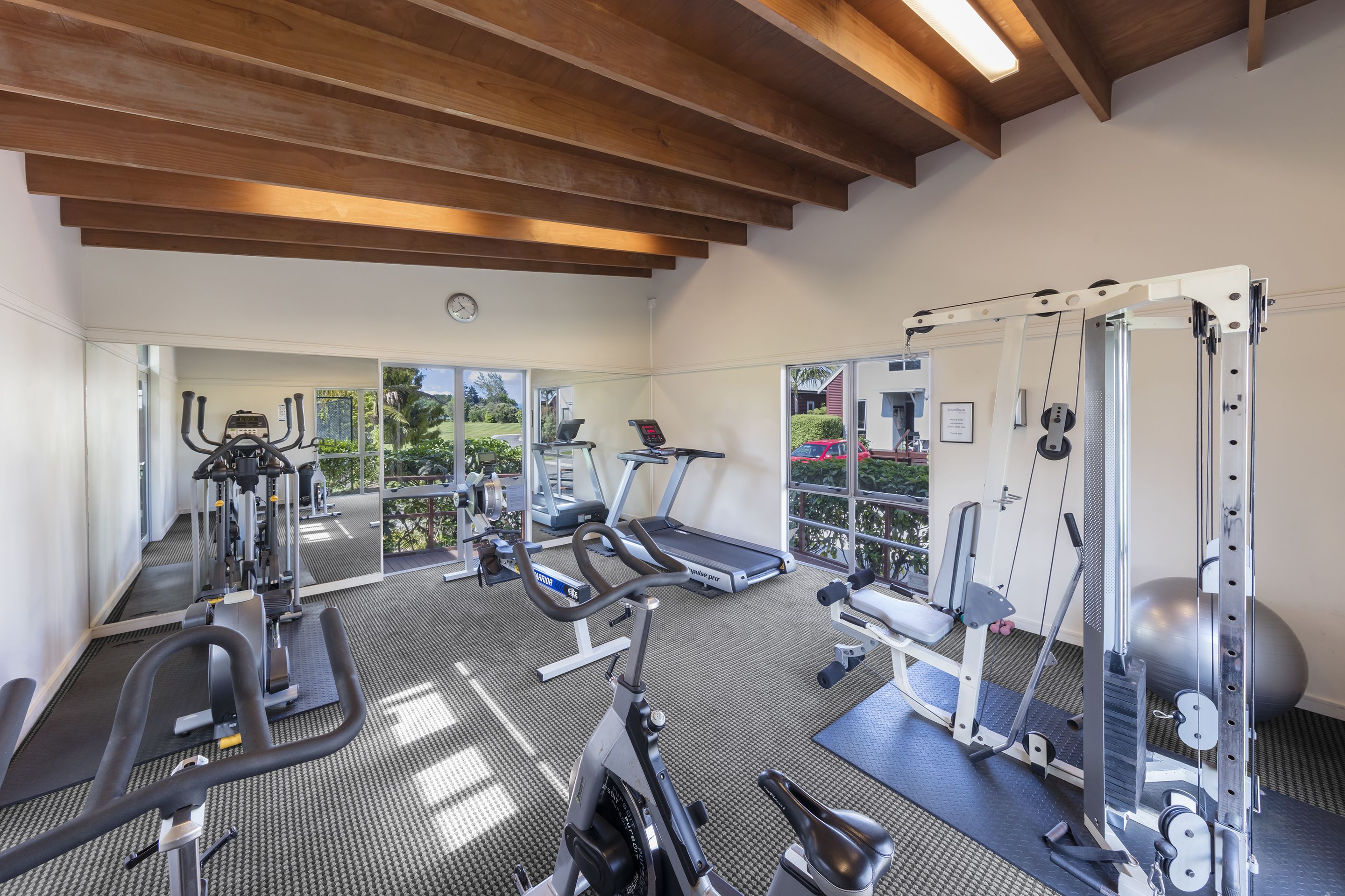 Una palestra con diverse attrezzature per l'allenamento, ampie finestre e un soffitto in legno.