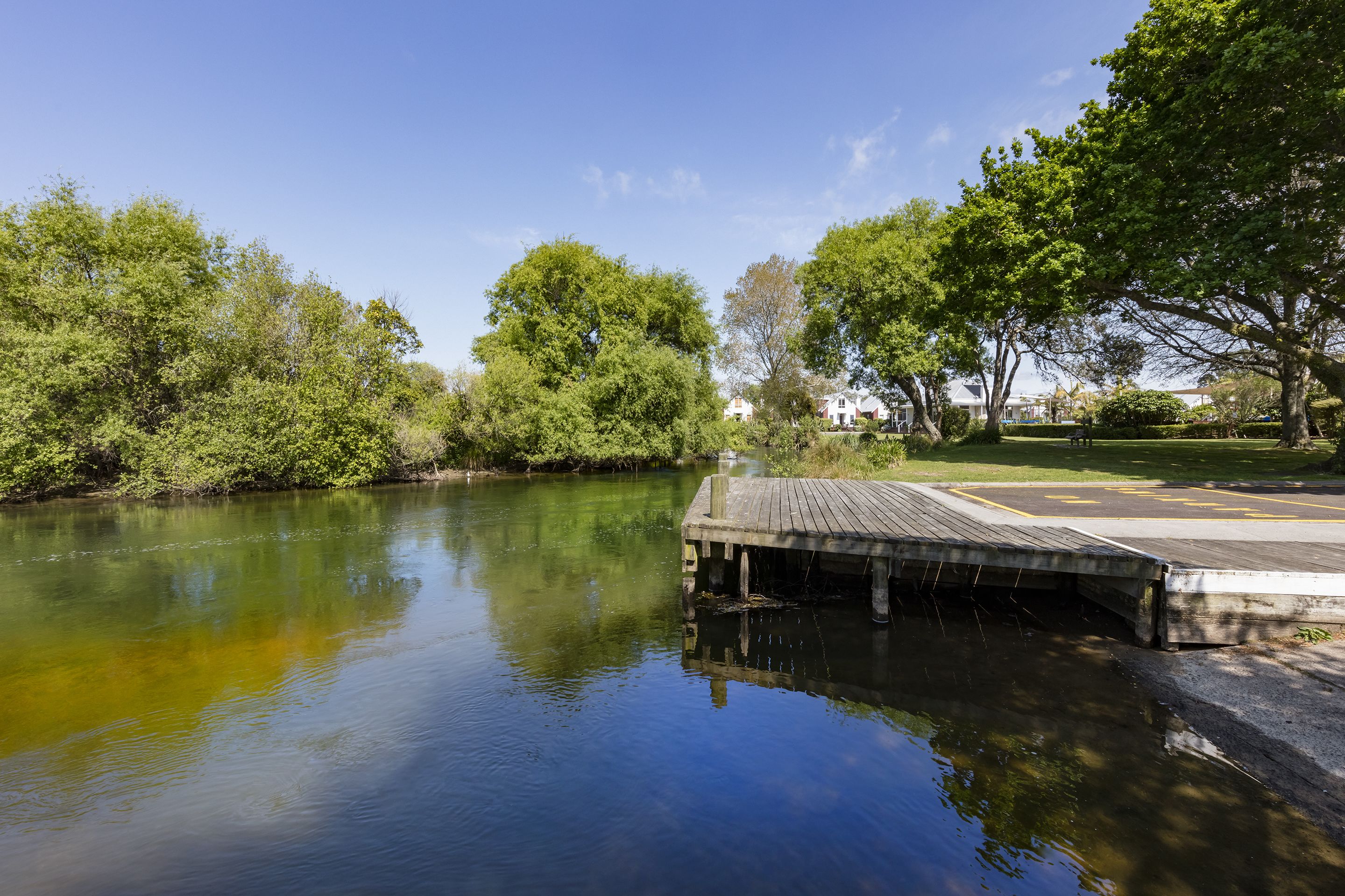 A calm river with a wooden dock extending into the water, surrounded by lush greenery and trees.