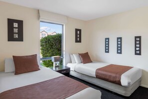 A hotel room with two beds, a window with a view of greenery, and artwork on the walls. - Ramada Resort By Wyndham Rotorua Marama (Mourea)