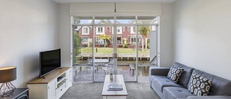 A modern living room with a large window, a flat-screen TV, a sofa, a coffee table, and a fireplace.