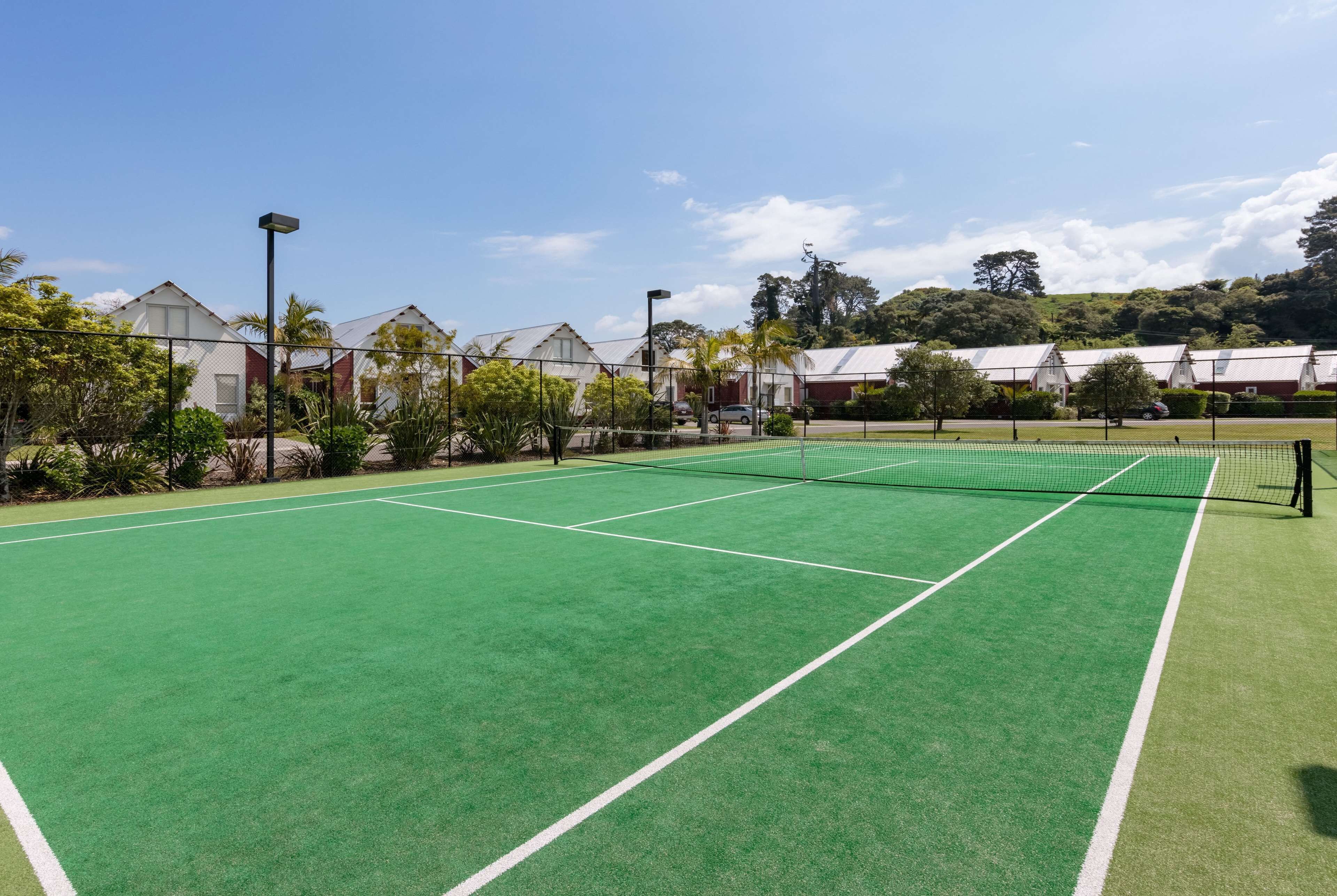 Een tennisbaan met een net, omringd door groen en gebouwen.
