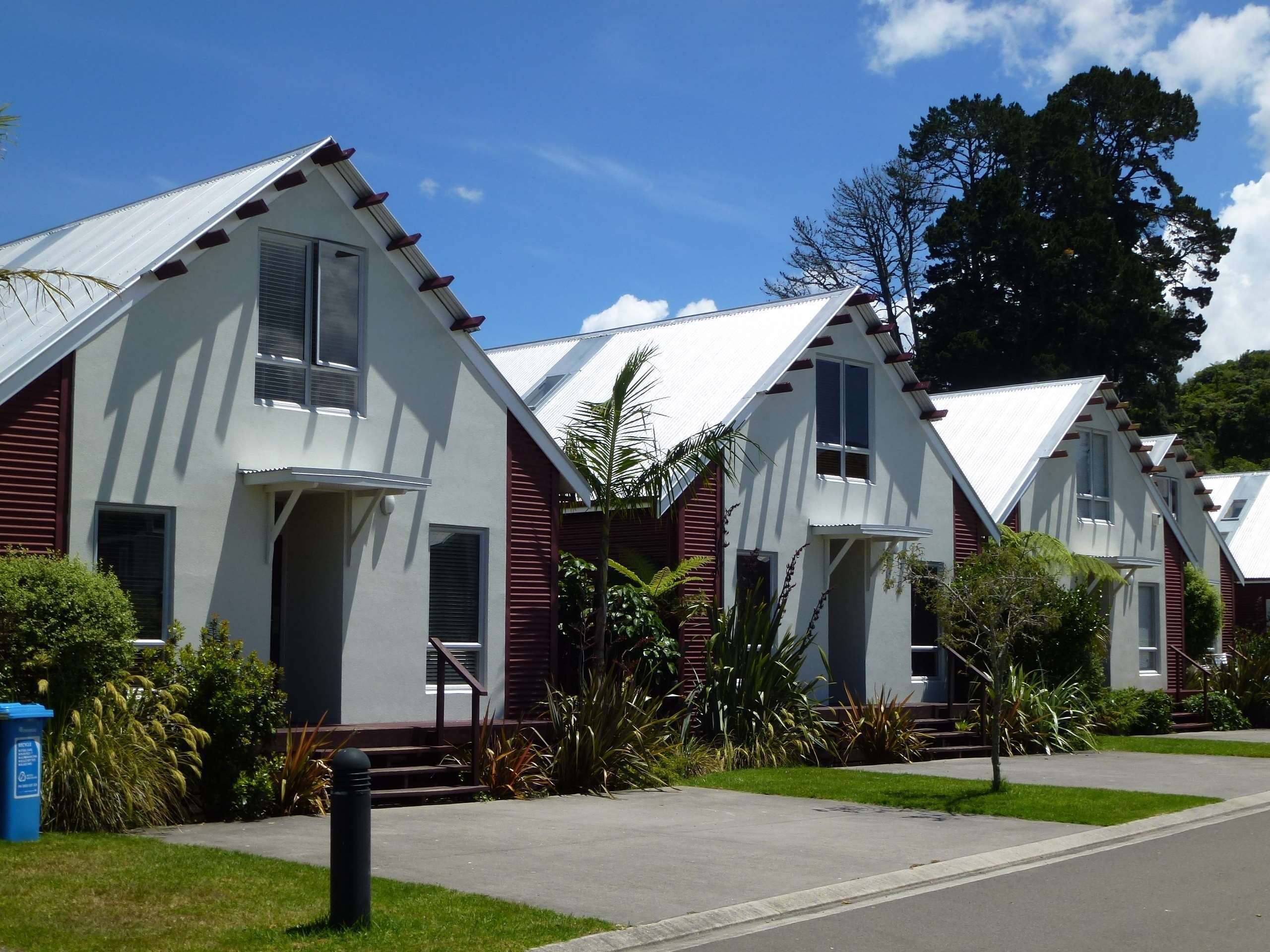 Une rangée de maisons modernes à un étage, toutes construites dans un style architectural uniforme, avec des toits en pente et un revêtement extérieur combinant des couleurs blanche et bordeaux.