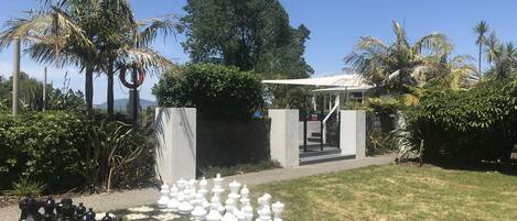 A chessboard set up outdoors with a garden and a building in the background.