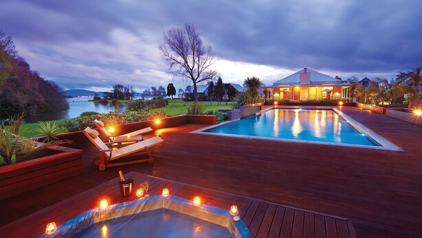 Un área de piscina exterior lujosa con un jacuzzi, sillas de descanso y vistas a un lago al atardecer.