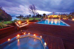 A luxurious outdoor pool area with a hot tub, lounge chairs, and a view of a lake at dusk. - Ramada Resort By Wyndham Rotorua Marama (Mourea)