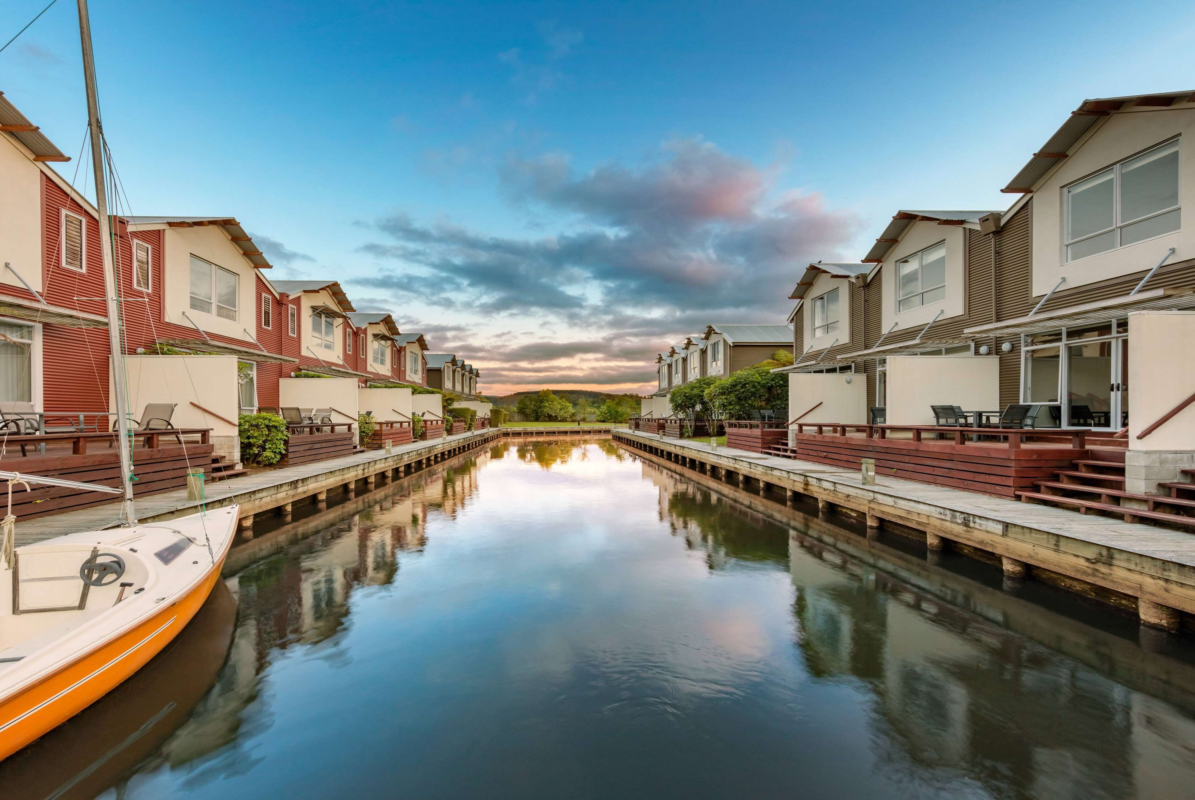 Un canal, avec un bateau amarré sur la rive gauche, bordé de bâtiments modernes dotés de balcons et d’espaces de détente en plein air.