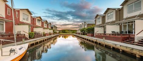 Un canal, avec un bateau amarré sur la rive gauche, bordé de bâtiments modernes dotés de balcons et d’espaces de détente en plein air.